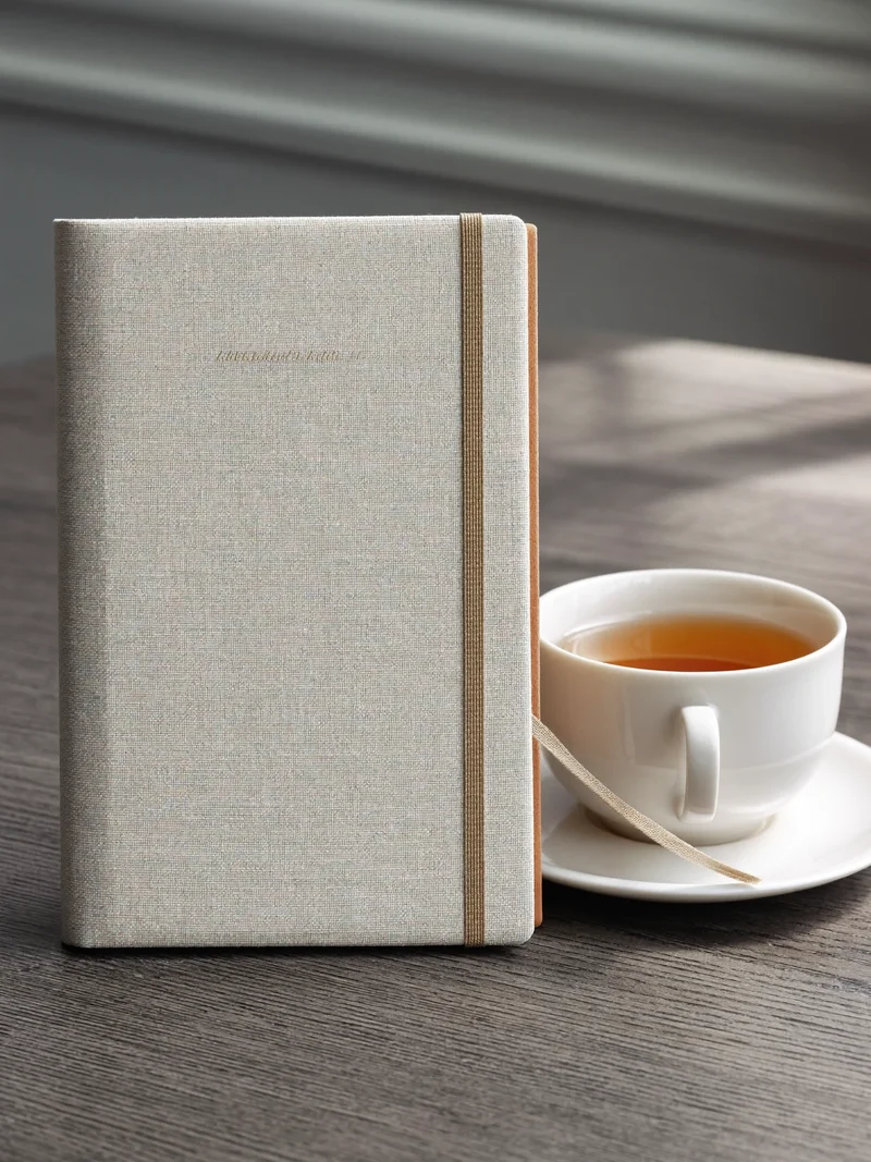 Journal en lin avec élastique et signet ruban posé près d'une tasse de thé
